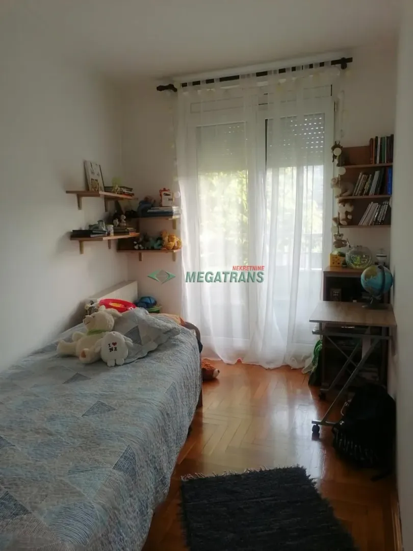 Dečja soba sa krevetom, radnim stolom i policama.
