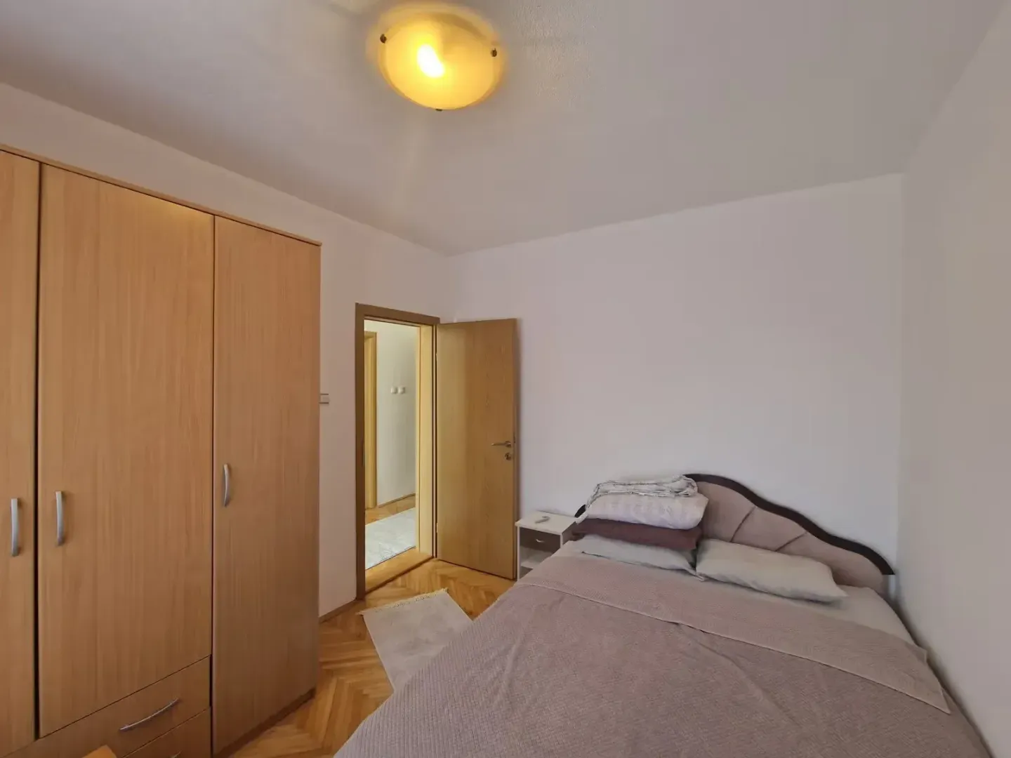 Bedroom with a double bed, large wooden wardrobe, and parquet flooring.