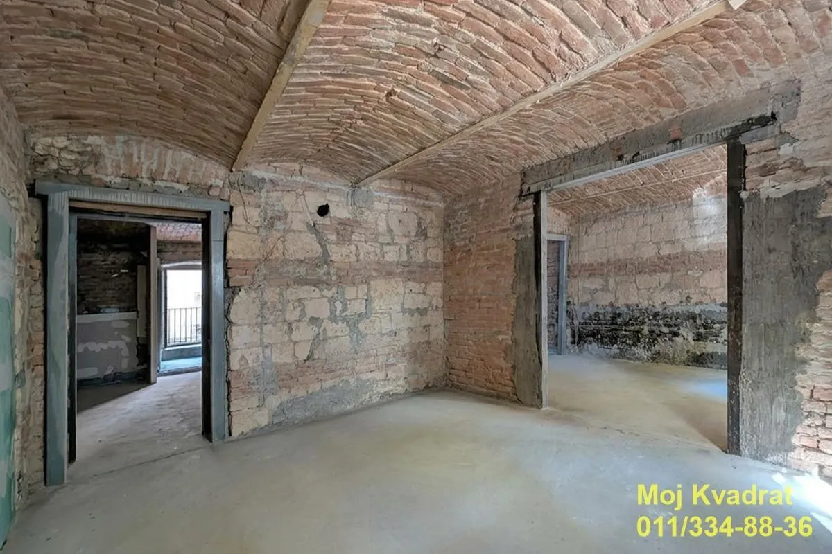 Nenamještena prostorija u sivoj fazi sa kamenim zidovima i svodnim plafonom od cigle.