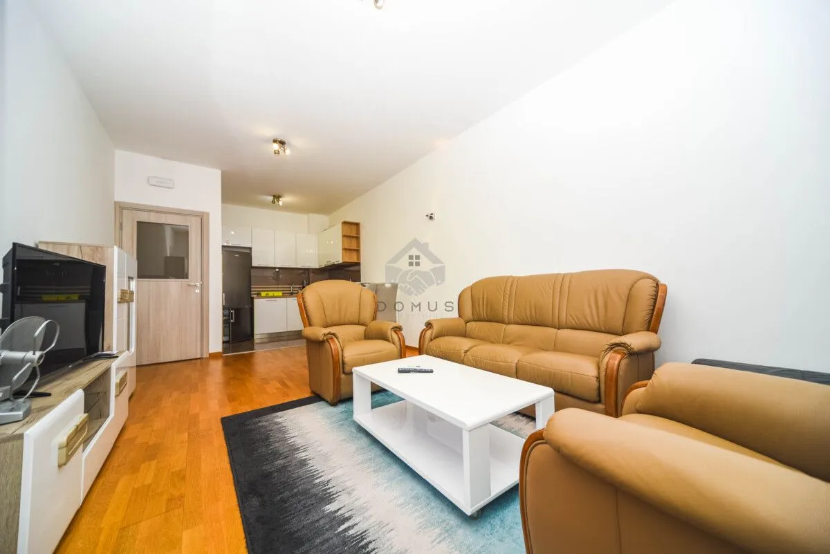 Living room with a sofa set and television, with a view of the kitchen in the background.