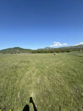 Pogled na prostrano zeleno zemljište sa brdima u pozadini. - image 3