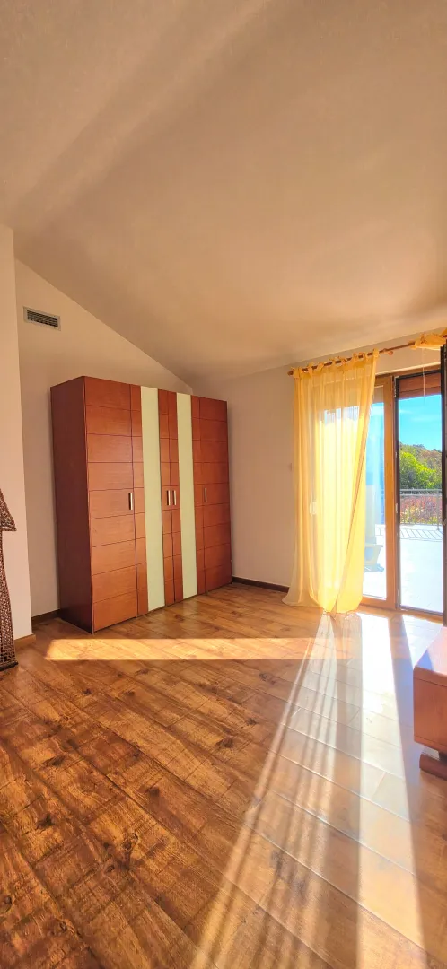 Bright bedroom with wooden flooring, a large wardrobe, and access to the terrace.