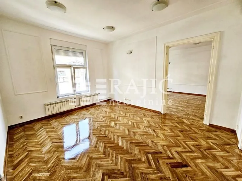 Empty room with parquet flooring and a large window.