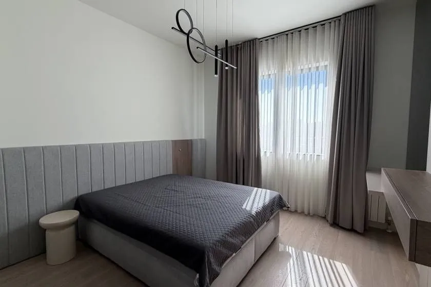 Moderna spavaća soba sa bračnim krevetom, tapaciranim uzglavljem i velikim prozorom.