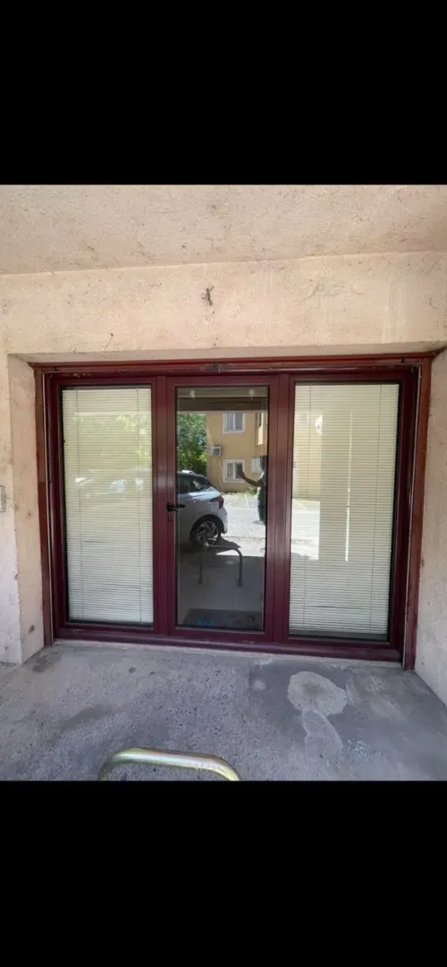 Entrance door with dark frame and blinds.