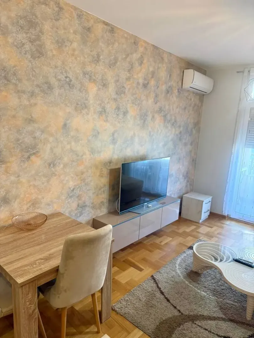 Dnevna soba sa garniturom, TV-om i trpezarijskim stolom.