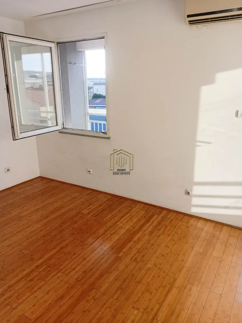 Empty room with wooden flooring and an open window.