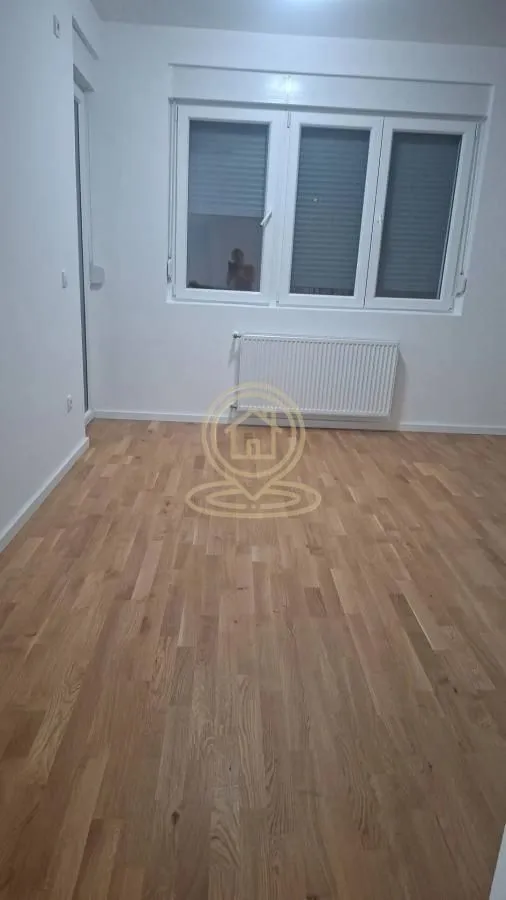 Prazna soba sa parketom i belim zidovima.