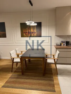 Trpezarija sa stolom, stolicama i modernim osvjetljenjem, sa dijelom kuhinje u pozadini. - image 6