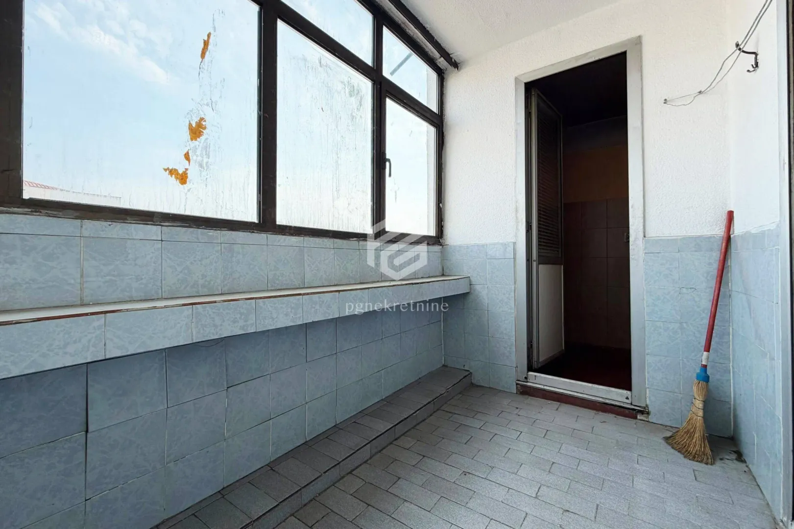 Zastakljeni balkon sa pločicama i vratima koja vode u unutrašnjost.