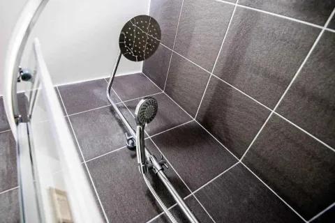 Krupni kadar tuš kabine sa tamnim pločicama i modernom slavinom. - image 9