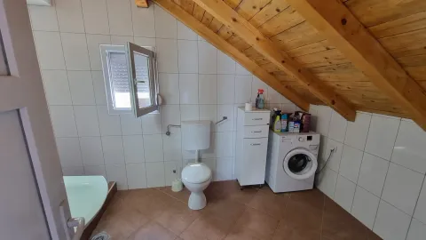 Kupatilo u potkrovlju sa wc šoljom, mašinom za veš i drvenim krovnim gredama. - image 10