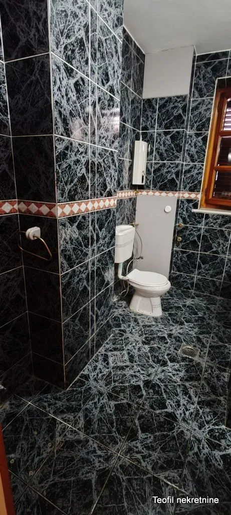 Bathroom tiled with dark marble tiles featuring a toilet.