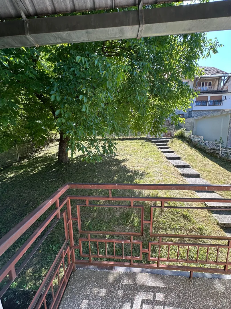 Pogled sa terase na zeleno dvorište i okolne kuće.