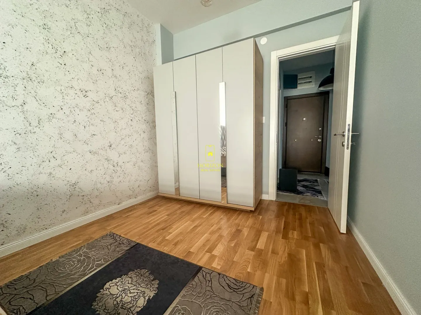 Manja spavaća soba sa velikim bijelim ormarom i drvenim podom.
