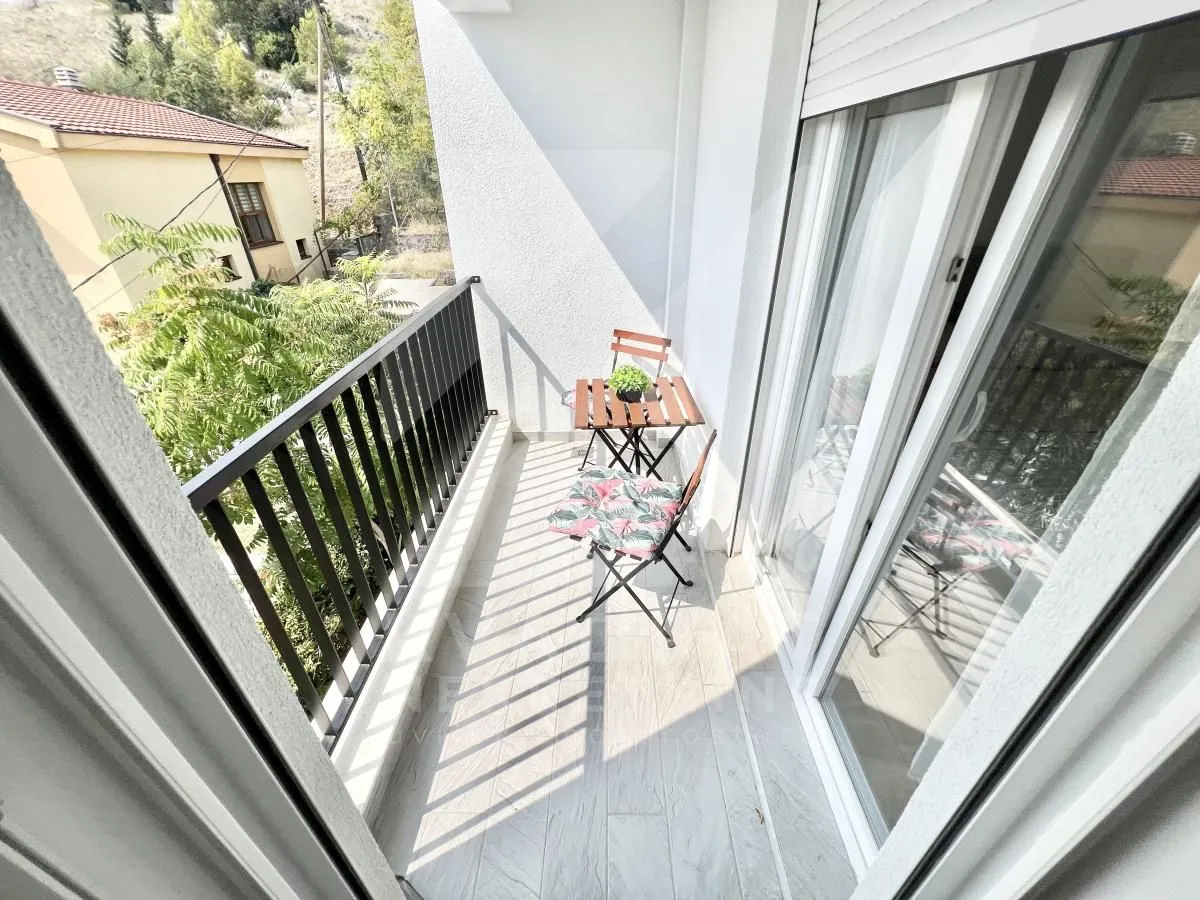 Manji namješteni balkon sa stolom i stolicama i pogledom na okolinu.