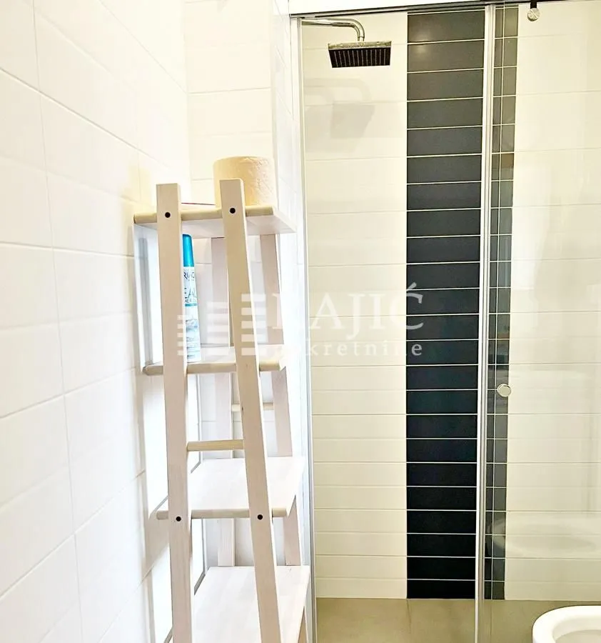 View of a modern bathroom with a glass shower cabin and a wooden shelf.