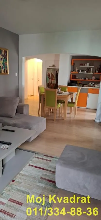 Prostrani dnevni boravak sa garniturom i trpezarijom u pozadini.