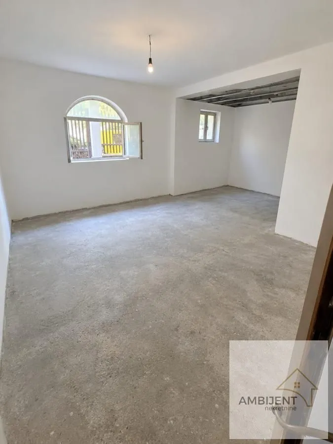 Prazna prostorija u kući sa belim zidovima i nezavršenim plafonom.