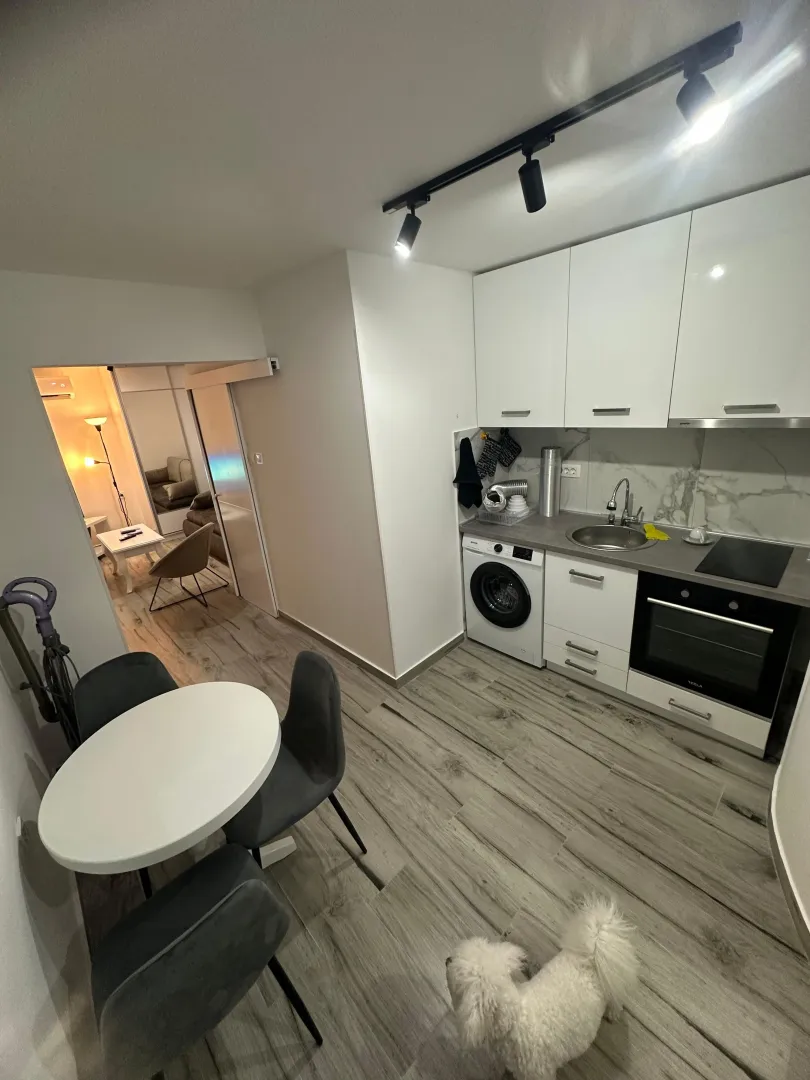 Kitchen equipped with white cabinets, featuring a dining table and a view of the living room.