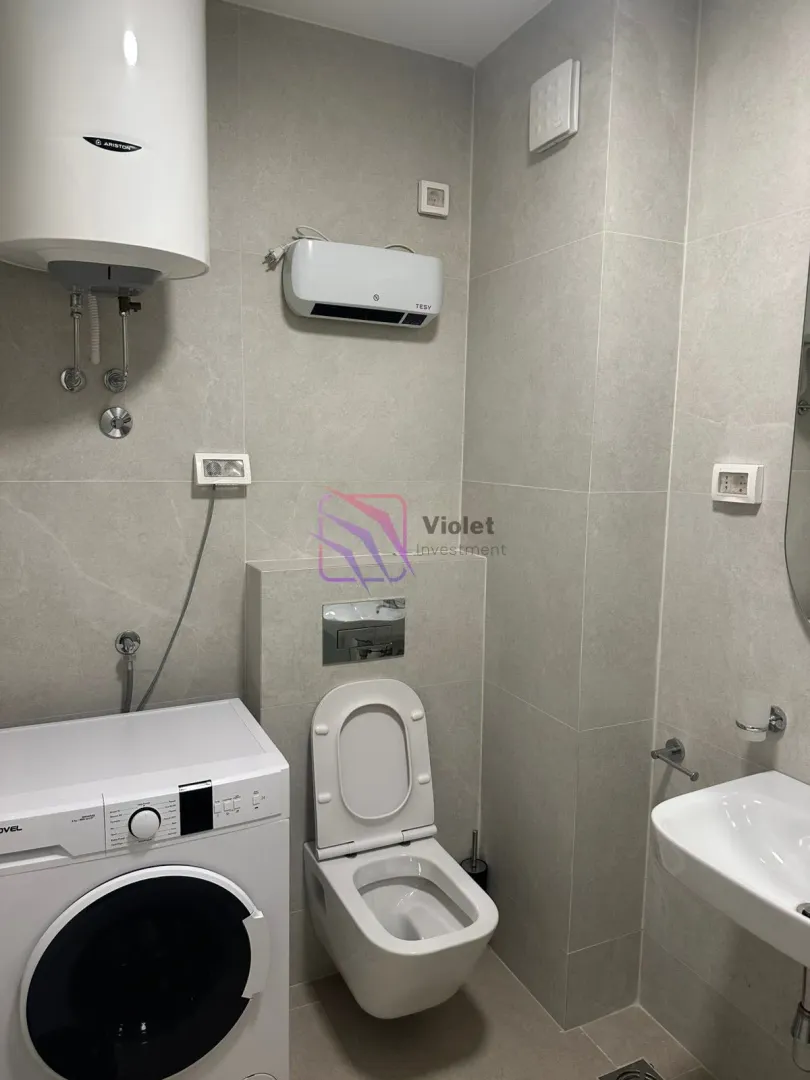 Modern bathroom with a toilet, washbasin, water heater, and washing machine.