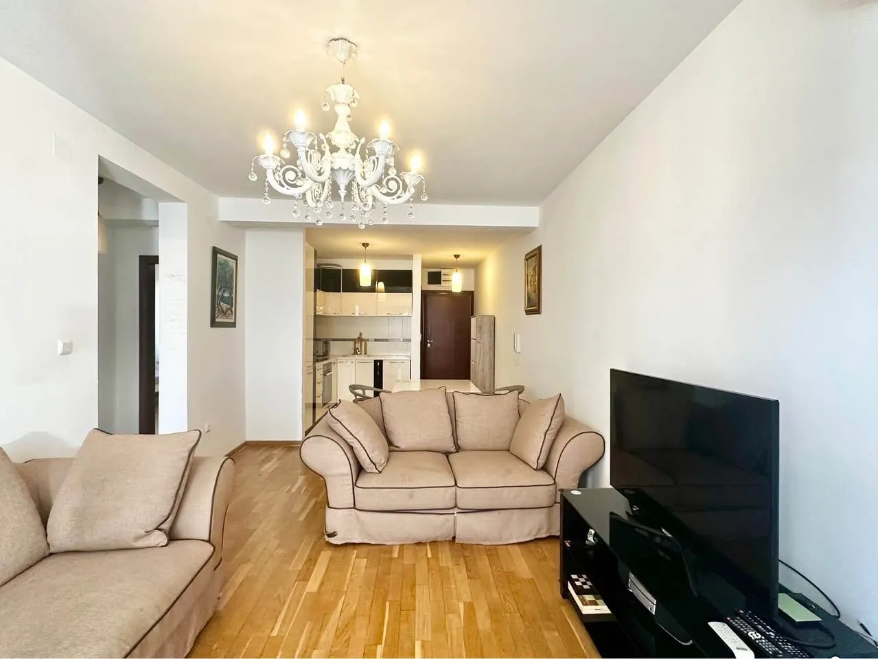 Living room with sofa, TV and a view towards the kitchen and entrance.