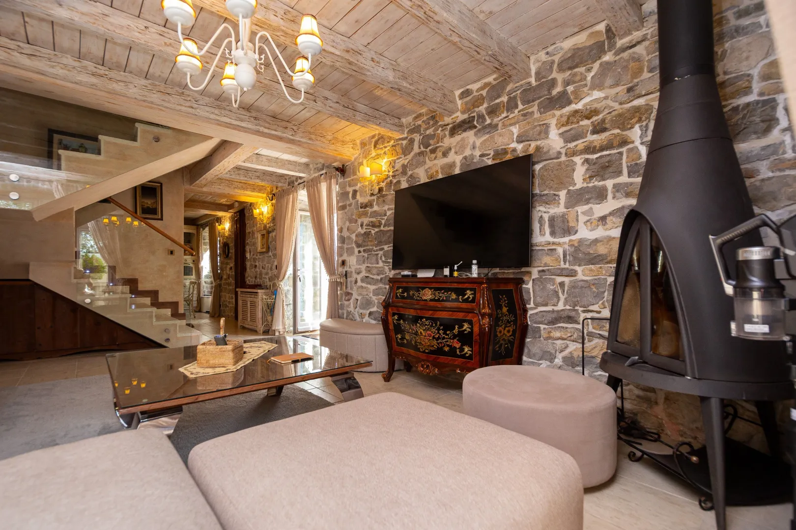 Spacious living room with a stone wall, fireplace, and exposed wooden ceiling beams.