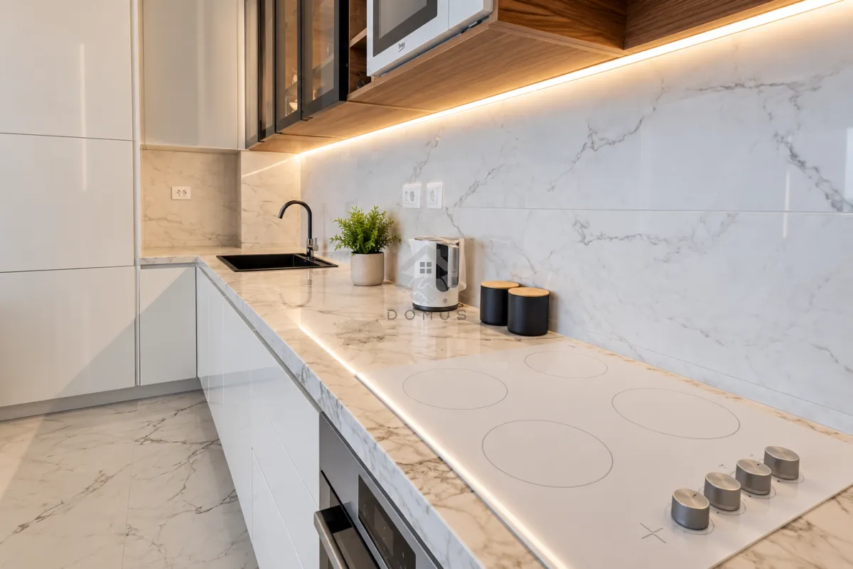 Modern kitchen with a marble countertop, built-in cooktop, and sink.