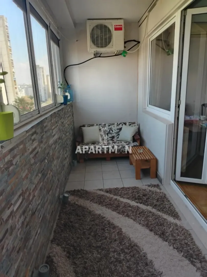 Enclosed balcony with a bench, small table, and rug.
