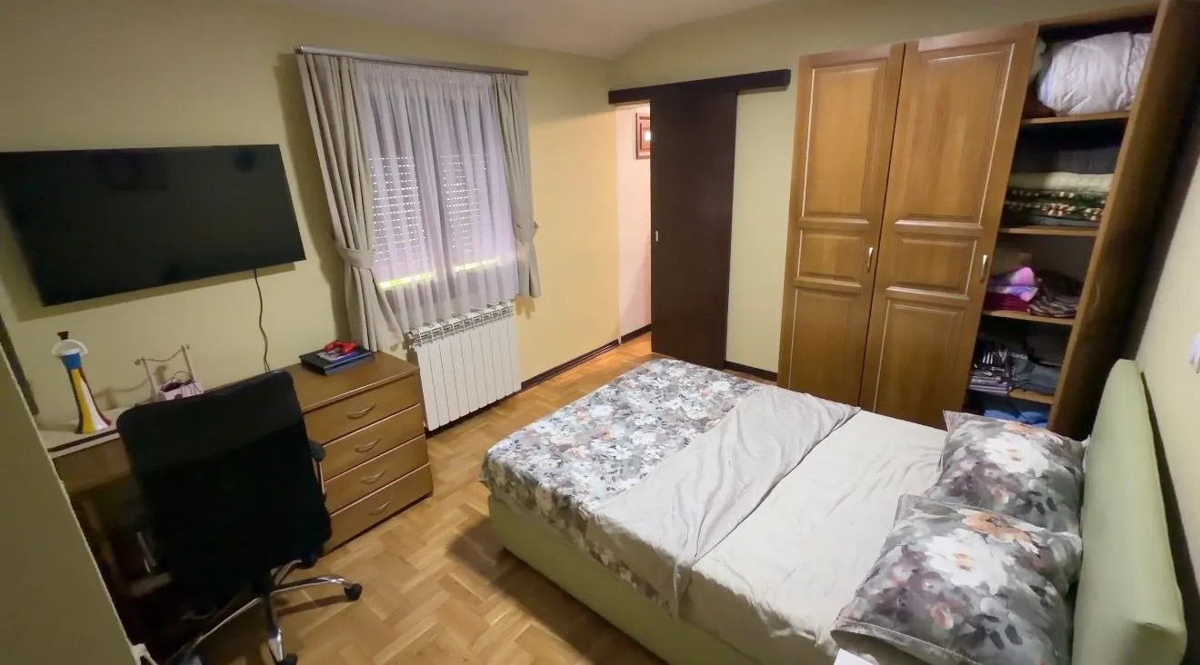 Namještena spavaća soba sa bračnim krevetom, plakarom, radnim stolom i televizorom.