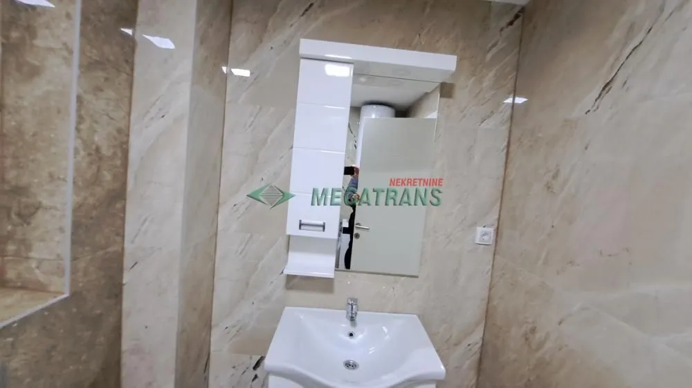 Kupatilo obloženo keramičkim pločicama sa umivaonikom i ogledalom.