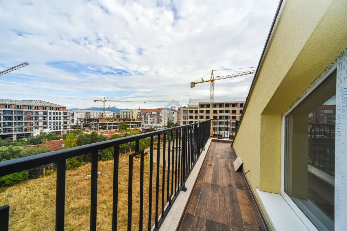 Dugački balkon sa drvenim podom i pogledom na gradilište.