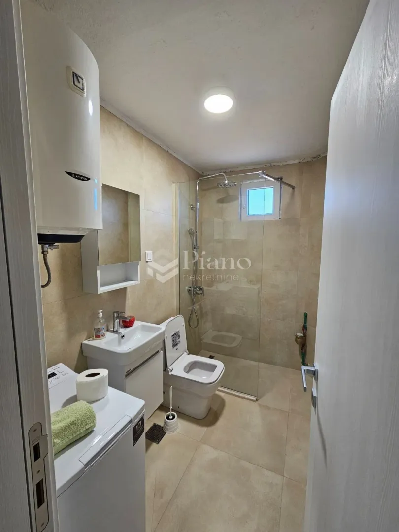 Small bathroom with a shower cabin, washbasin, toilet, and water heater.
