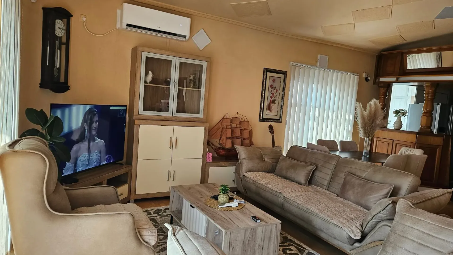 Furnished living room with sofa, television, and dining area in the background.