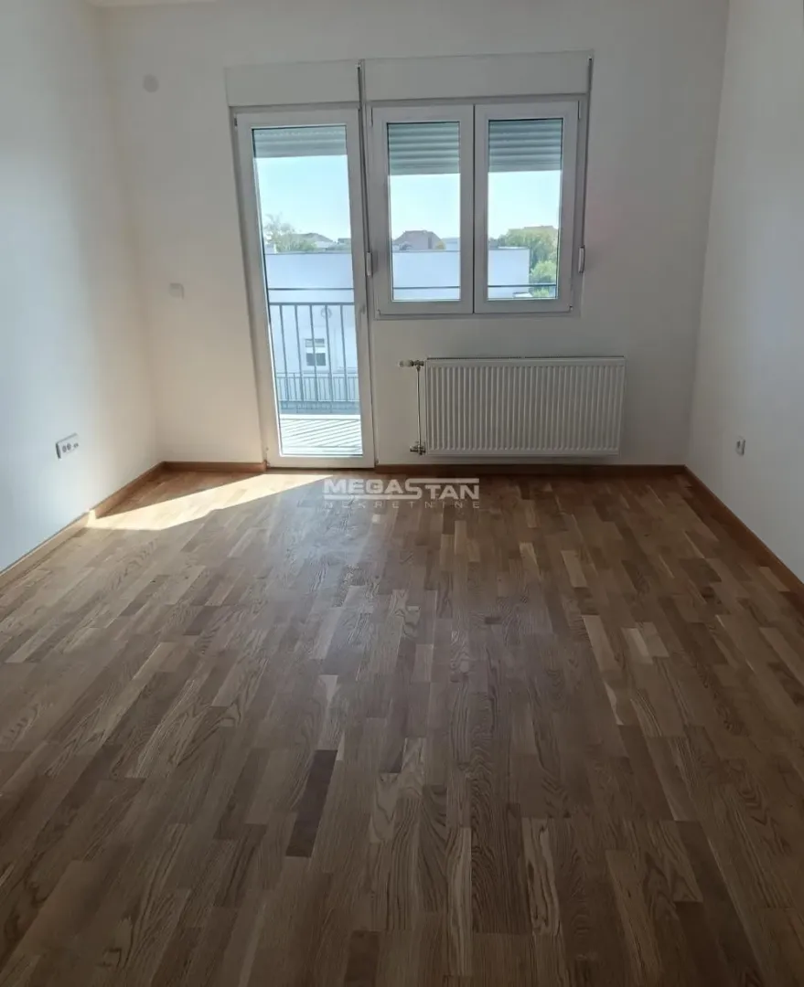 Prazna neopremljena soba sa drvenim podom i balkonskim vratima.
