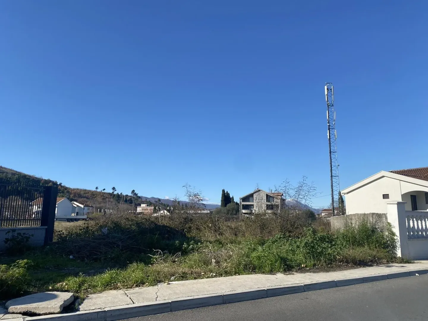 Pogled na neizgrađeni plac pored puta sa okolnim kućama.