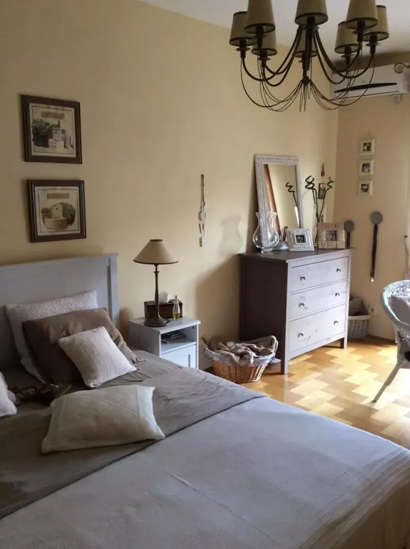 Udobna spavaća soba sa bračnim krevetom, komodom i detaljima na zidovima.