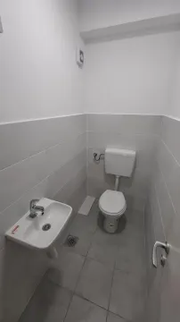 Manje kupatilo sa WC šoljom i umivaonikom obloženo svetlim pločicama. - image 16