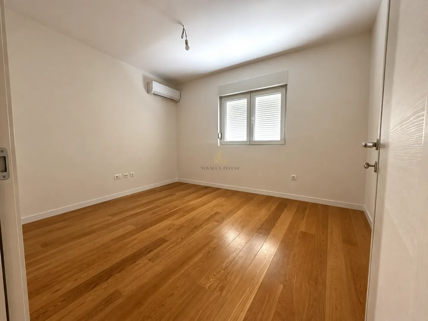 Empty room with hardwood flooring, white walls, and an air conditioning unit.