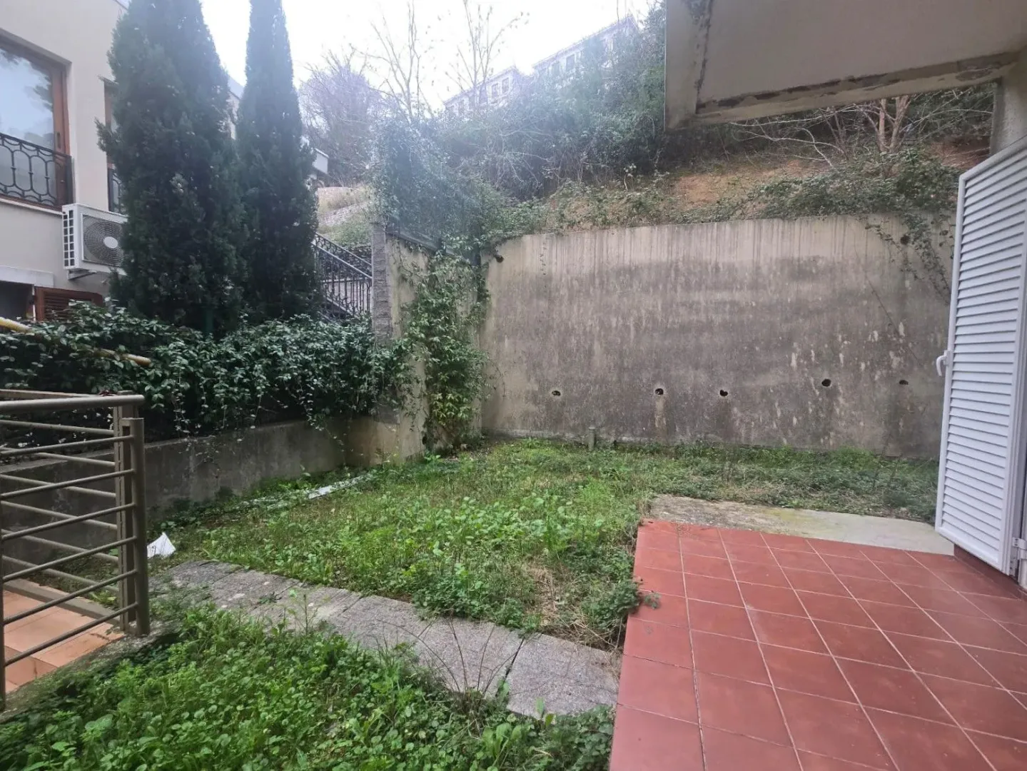Small grassy yard with a tiled patio area and fence.