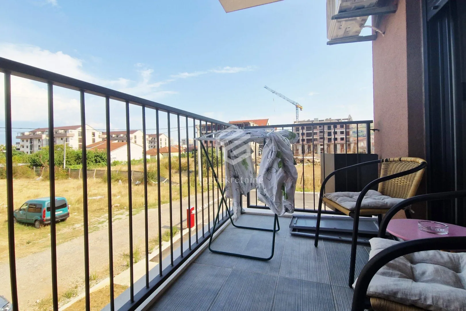 Small furnished balcony with seating furniture and a clothes drying rack.