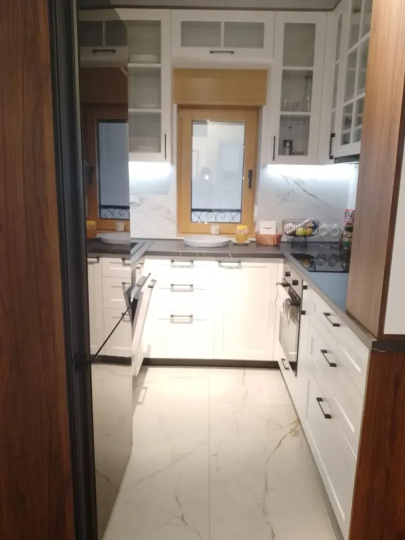 Pogled na moderno opremljenu kuhinju sa belim elementima i ugradnim uređajima.