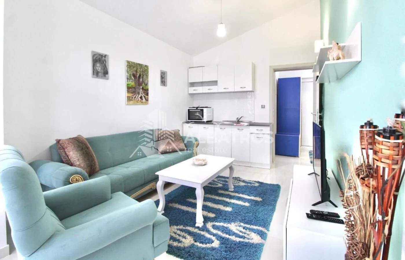 Living room with sofa set and a small kitchen in the background.