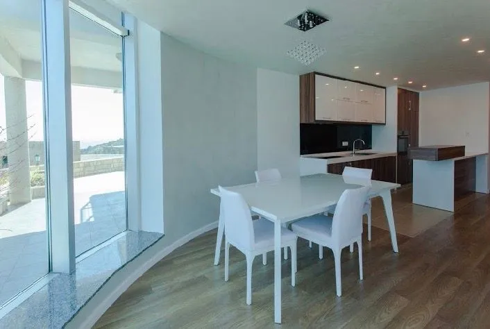 Open-plan living room with dining area and kitchen, featuring large windows.