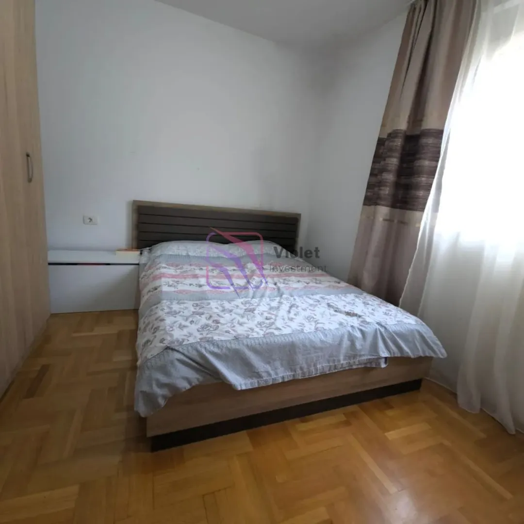 Spavaća soba sa bračnim krevetom, plakarom i prozorom sa zavjesama.