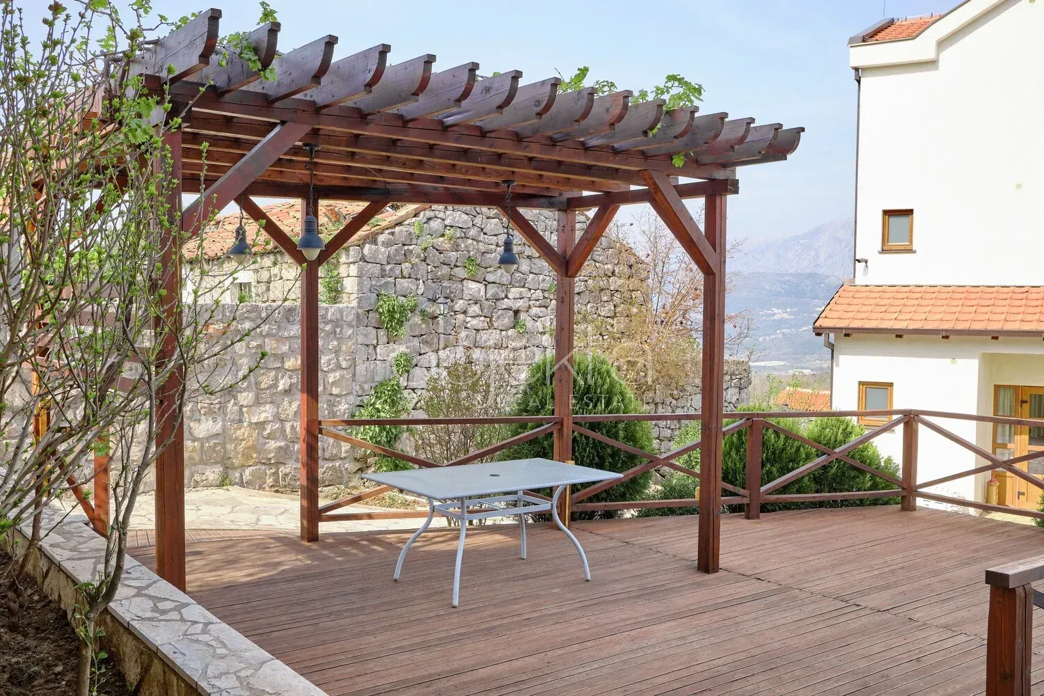 Drvena pergola sa stolom na prostranoj drvenoj terasi u dvorištu.