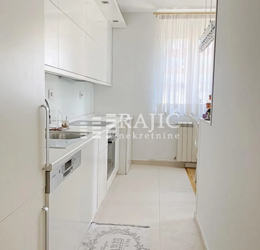 Modern white kitchen with built-in appliances and white floor tiles.
