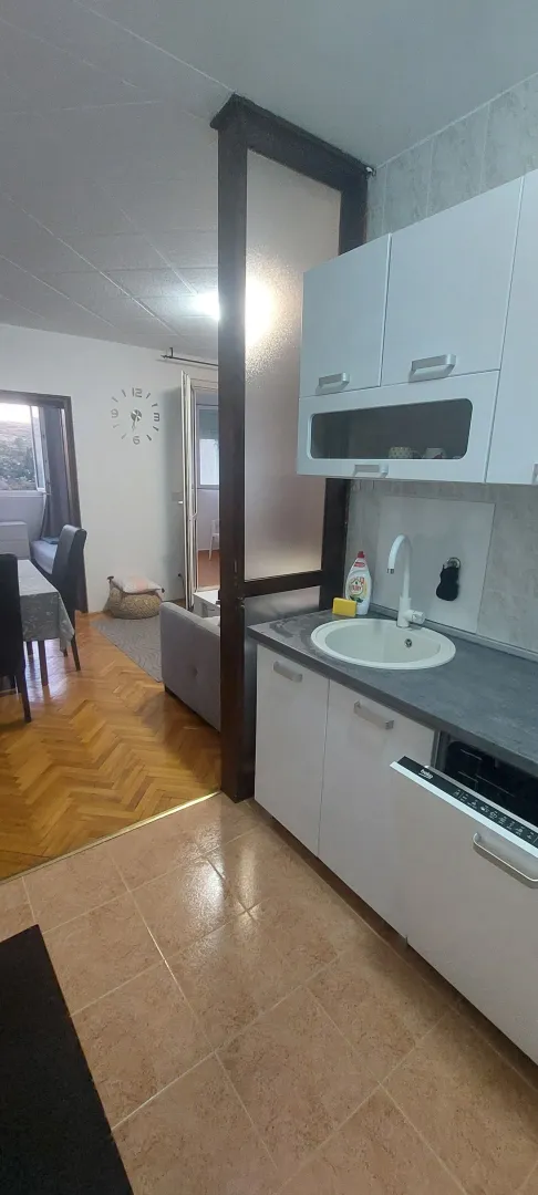 Prikaz kuhinje sa bijelim elementima i pogledom na hodnik i trpezariju.