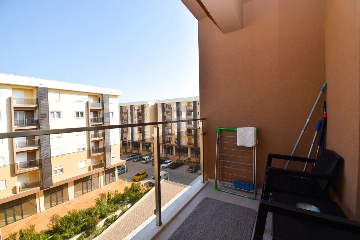 Manji namješteni balkon sa staklenom ogradom i pogledom na naselje.