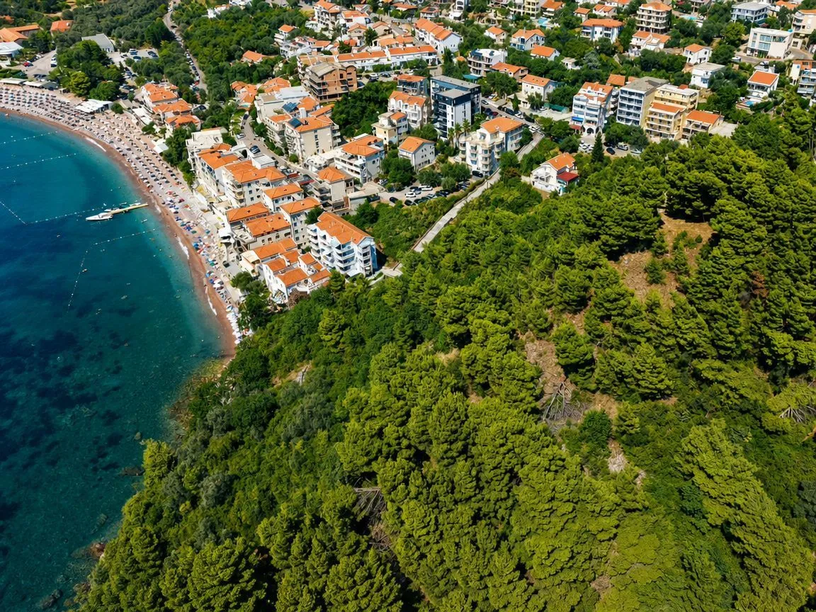 Pogled iz vazduha na obalu, naselje i šumu uz more.